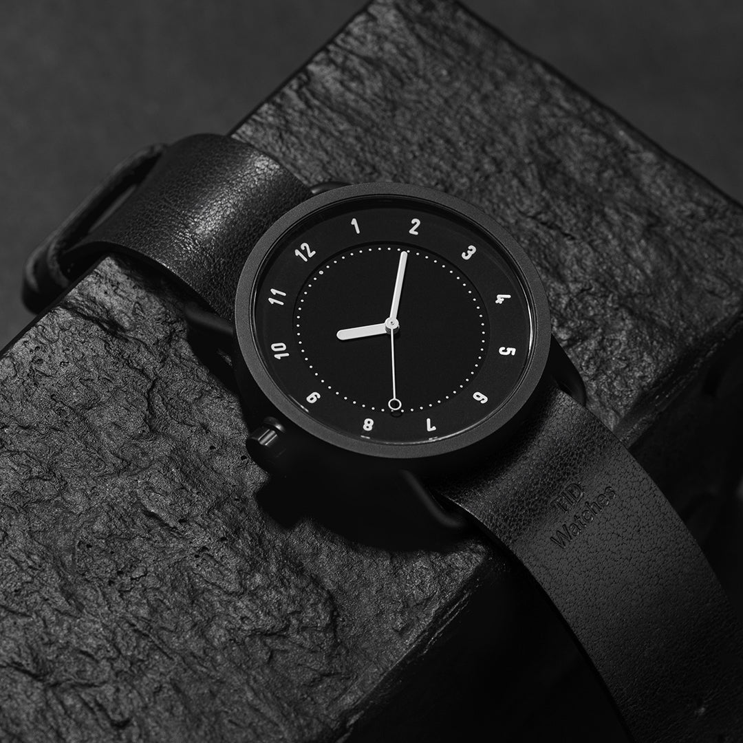 TID No.1 black dial minimalist watch with black leather strap on dark textured surface